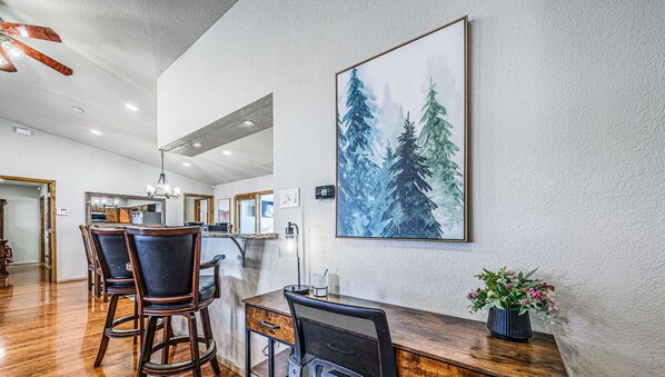 A dining area with a wooden table, chairs, and a large painting of trees. - Deer Creek Golf Cabin | Game Room & Wildlife Views (Ruidoso)