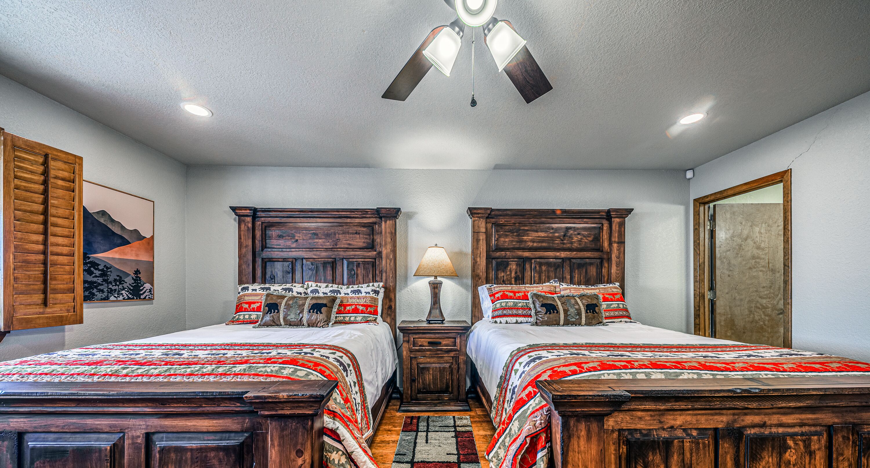 A bedroom with two wooden beds, a nightstand with a lamp, and a ceiling fan.