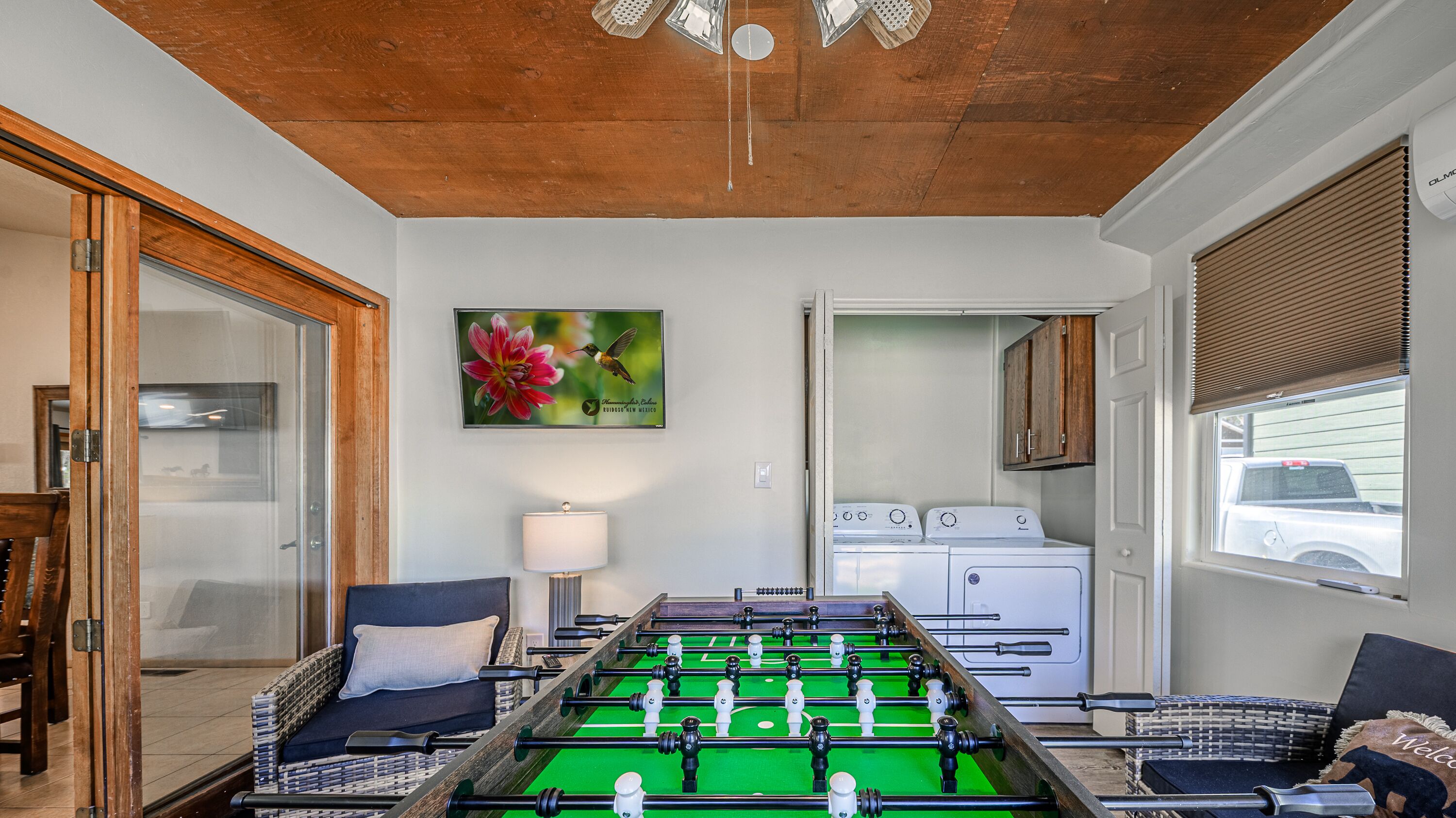A room with a foosball table, a washing machine, and a window with a view of a parked truck.