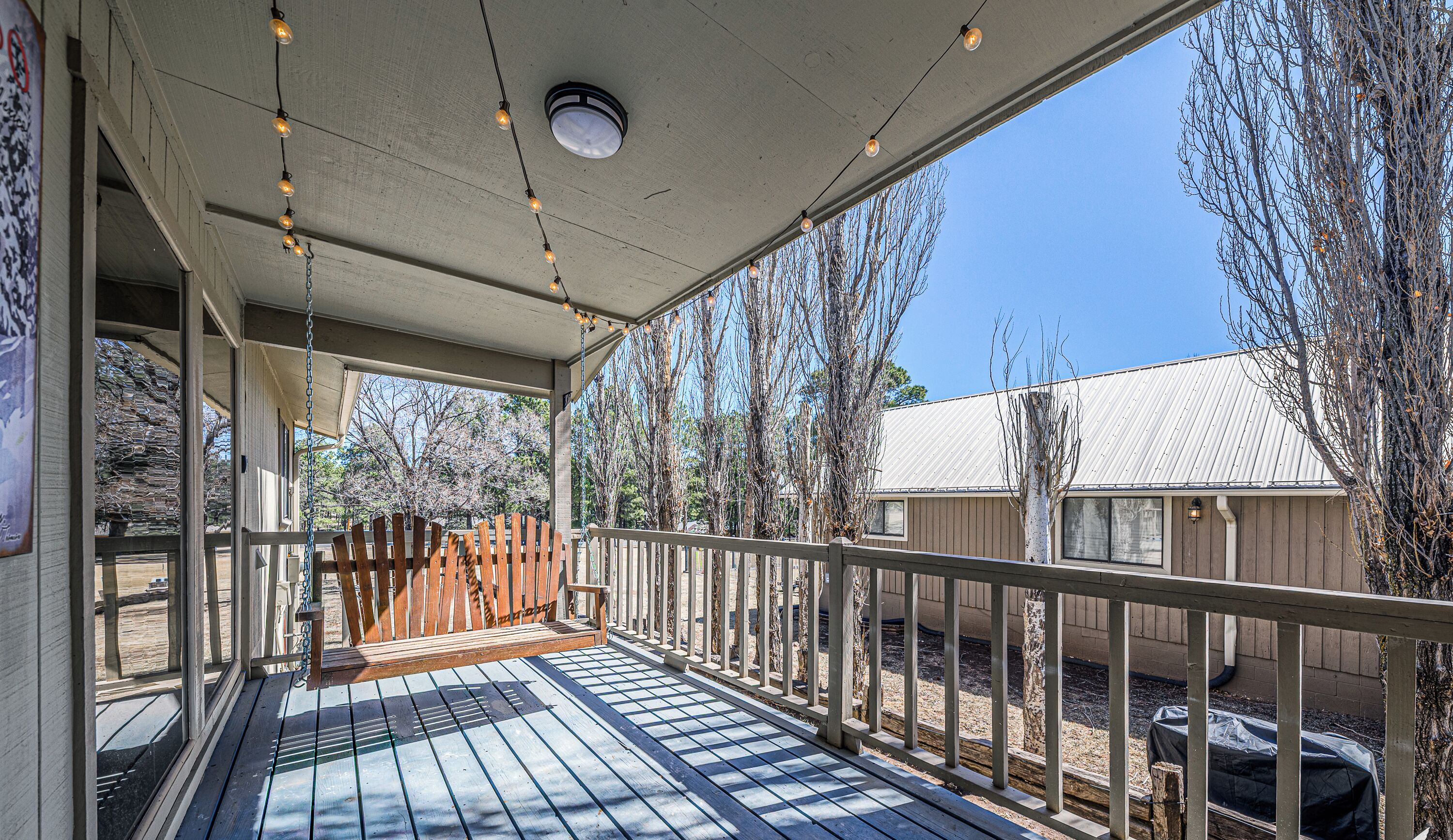 A covered outdoor deck with string lights, wooden benches, and a view of trees and buildings.