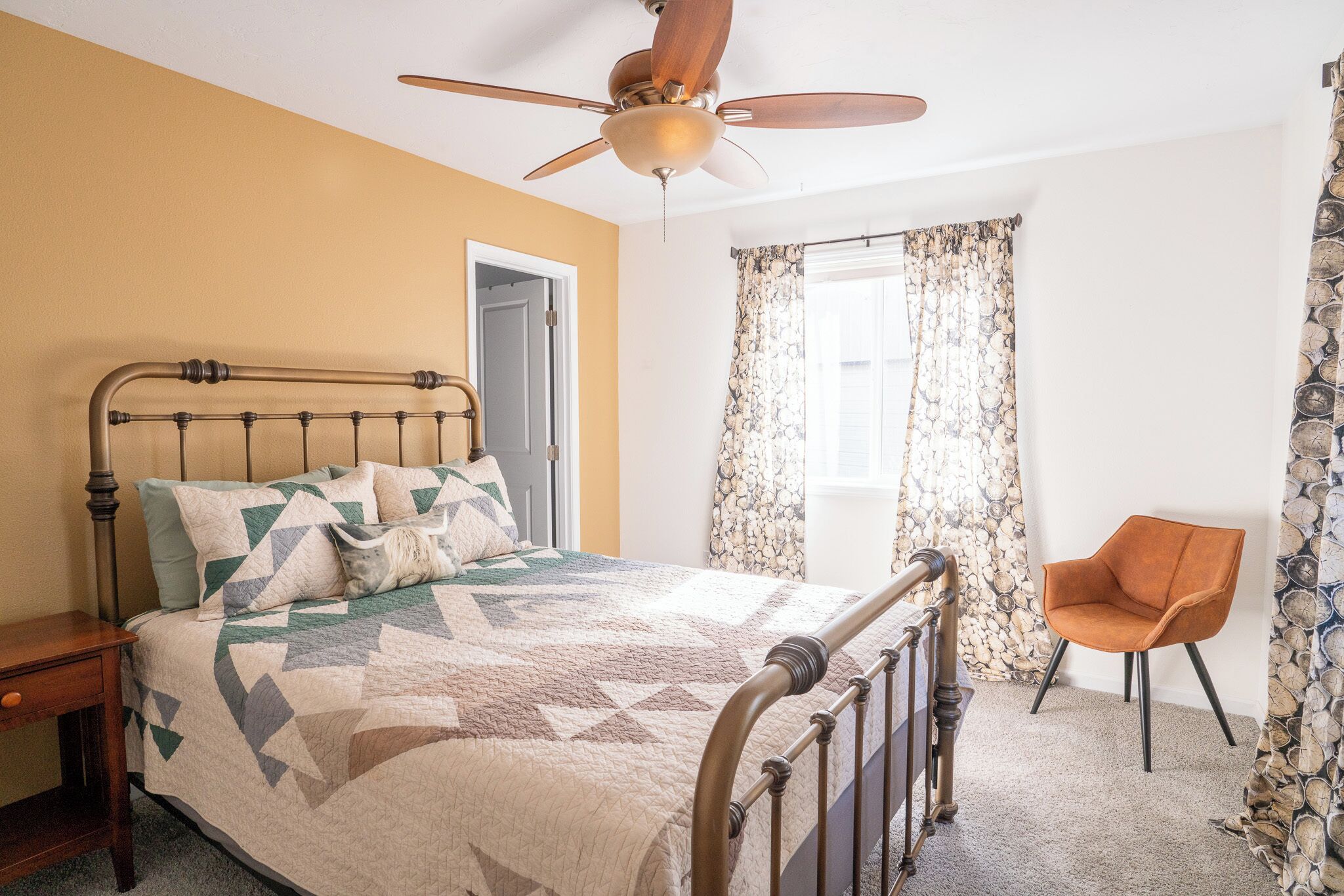 A bedroom with a bed, a chair, a ceiling fan, and a window with curtains.