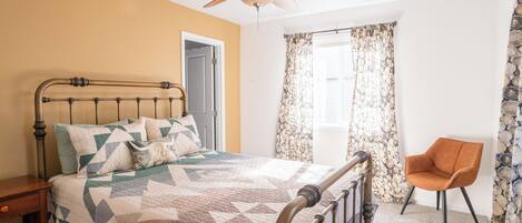 A bedroom with a bed, a chair, a ceiling fan, and a window with curtains.