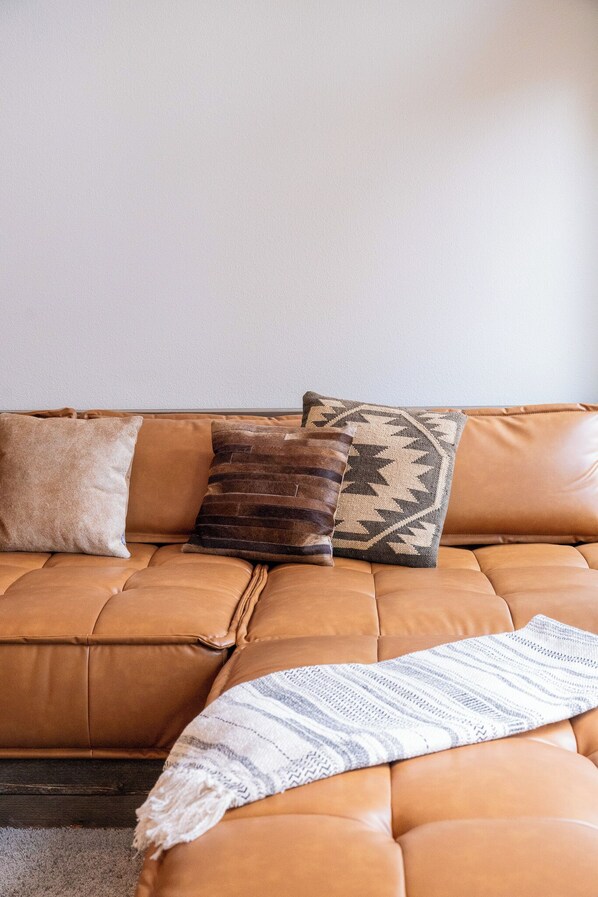 A brown leather sofa with three cushions, a striped throw blanket, and a plain wall in the background. - The L77 Ranch Hide-Out: A Forested Stay in Lyle, WA (Lyle)