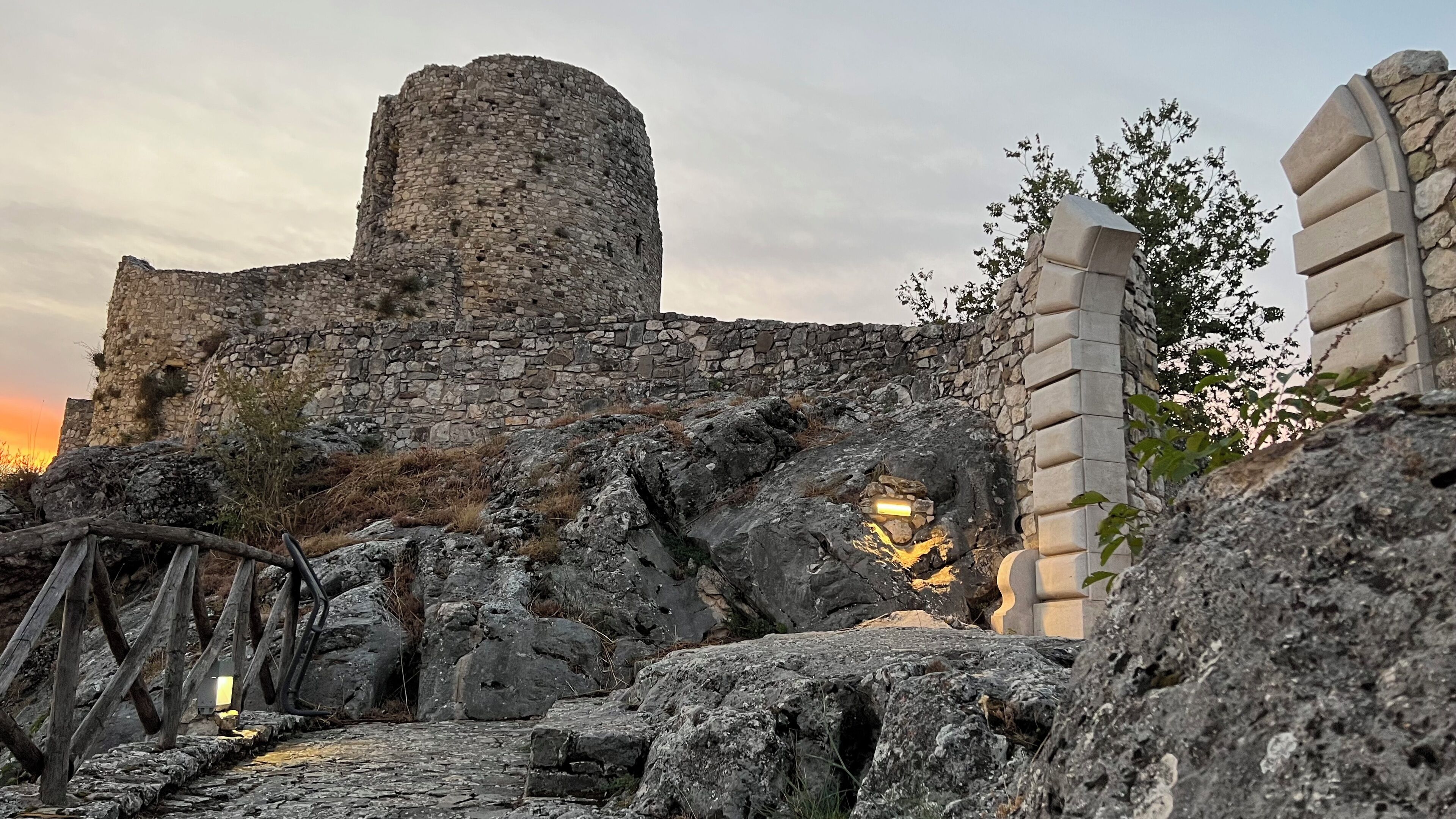 A stone castle ruin with a circular tower, a wooden bridge, and a stone gate.