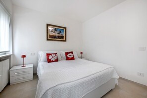 Quarto com cama, mesa de cabeceira, abajur e um quadro na parede.