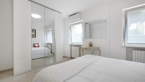 A bedroom with a bed, a wardrobe, a mirror, a radiator, and a window.