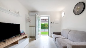 A modern living room with a flat-screen TV, a sofa, a wooden TV stand, and a door leading to a balcony.