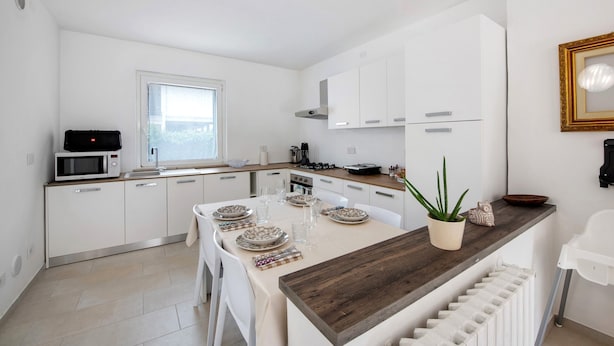 A modern kitchen with white cabinets, a wooden countertop, and a dining table set for four.