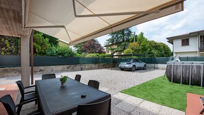 An outdoor patio with a table and chairs, a car parked in the background, and a green lawn.