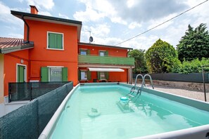 Uma piscina com escada, rodeada por uma casa com persianas verdes e fachada vermelha.