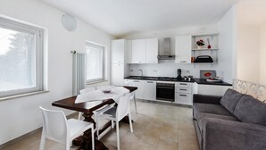 Una cocina moderna con armarios blancos, una mesa de comedor con sillas, un sofá gris y un radiador.
