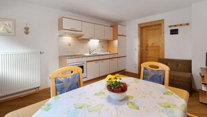 Una cocina compacta con armarios blancos, una puerta de madera y una mesa de comedor con mantel floral.