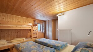 Una habitación de cabaña de madera con literas, una ventana con cortinas, un radiador y una lámpara fijada a la pared.