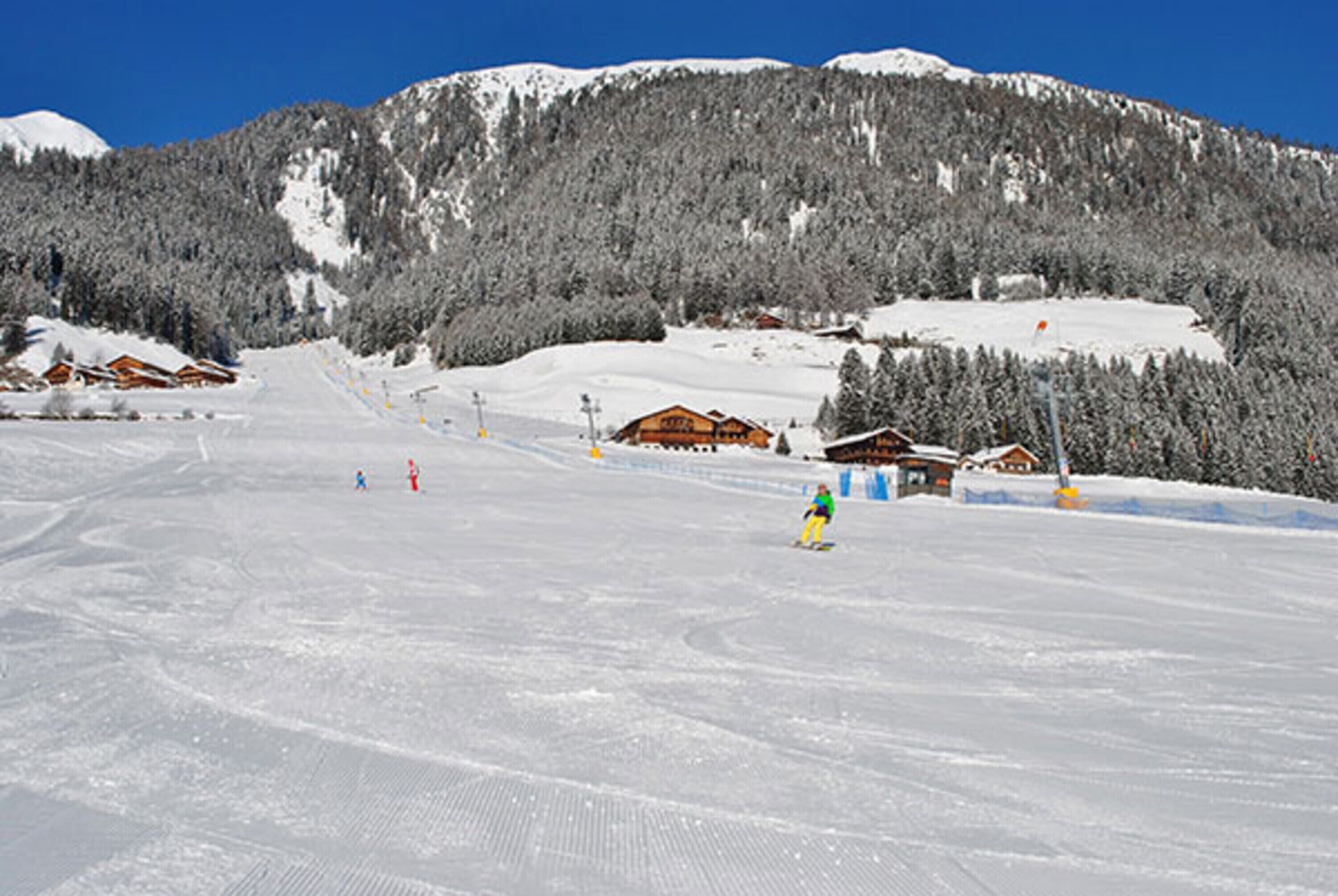 A snowy ski slope with wooden chalets and a clear blue sky.