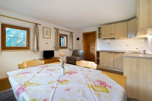 Ein Zimmer mit Esstisch, Stühlen, Fernseher, einer Couch und einer Küchenzeile mit Holzausbau und Spüle.