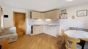 A compact kitchen with wooden cabinets, a dining table with chairs, and a sofa. - Apartment 'Rosenduft' with Mountain View, Shared Terrace and Wi-Fi (St. Magdalena gsies)