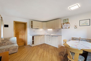 A compact kitchen with wooden cabinets, a dining table with chairs, and a sofa.