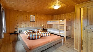 A wooden cabin room with bunk beds, a bed with a plaid blanket, a nightstand, and a wall-mounted lamp. - Apartment 'Rosenduft' with Mountain View, Shared Terrace and Wi-Fi (St. Magdalena gsies)