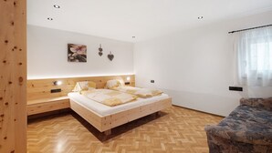 Quarto com cabeceira de madeira, cama com roupa de cama branca, piso com padrão herringbone e uma pequena mesa de cabeceira.
