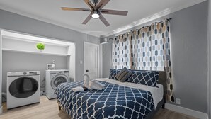 A bedroom with a bed, a ceiling fan, a washing machine, and a small potted plant. - Quirky & Stylish 3BR with Pool & Free Parking (Houston)