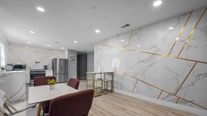 A modern kitchen with stainless steel appliances, a dining area with a marble wall and geometric gold accents, and a wooden floor. - Quirky & Stylish 3BR with Pool & Free Parking (Houston)