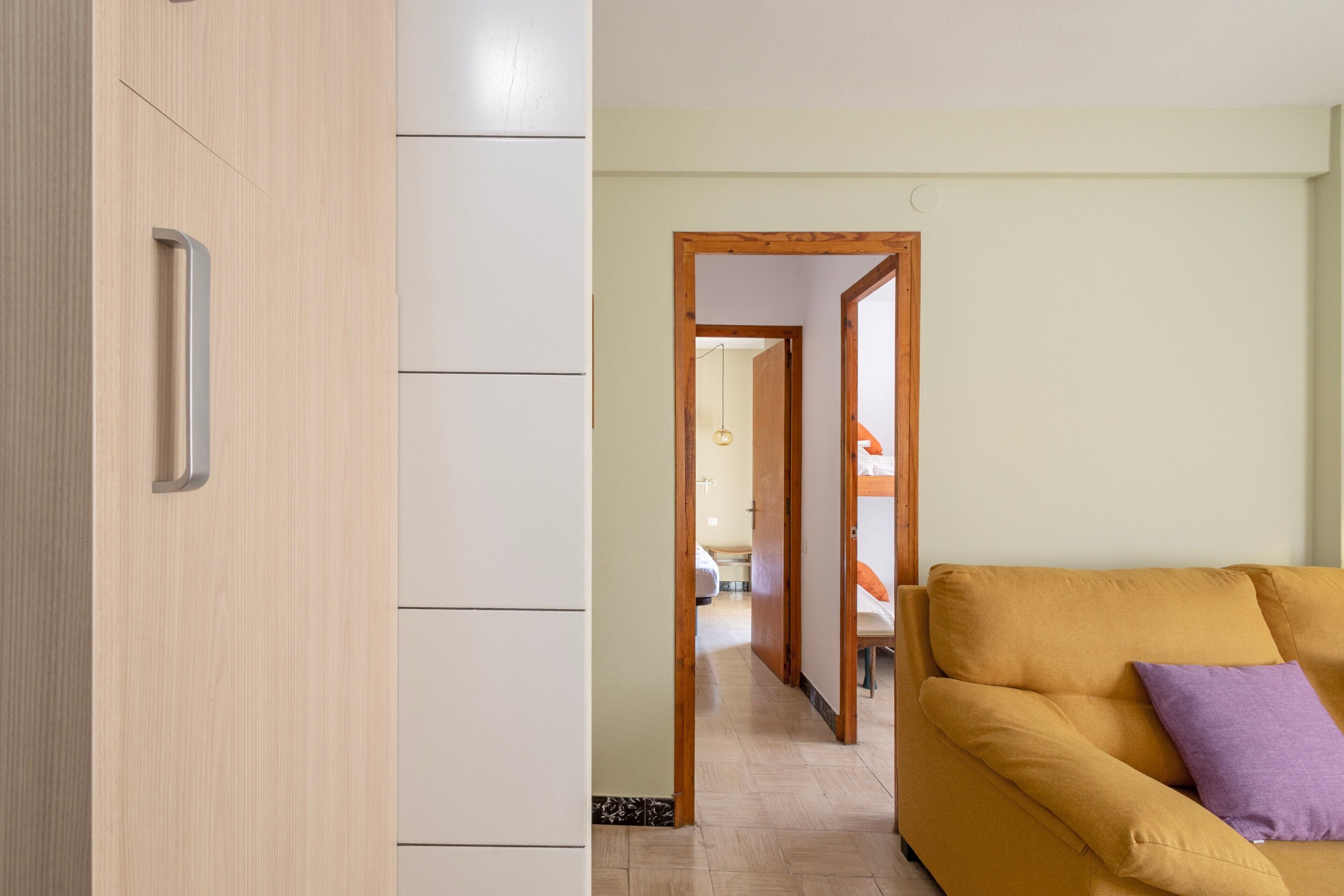 A modern room with a wooden wardrobe, a sofa with a cushion, and a hallway leading to another room.