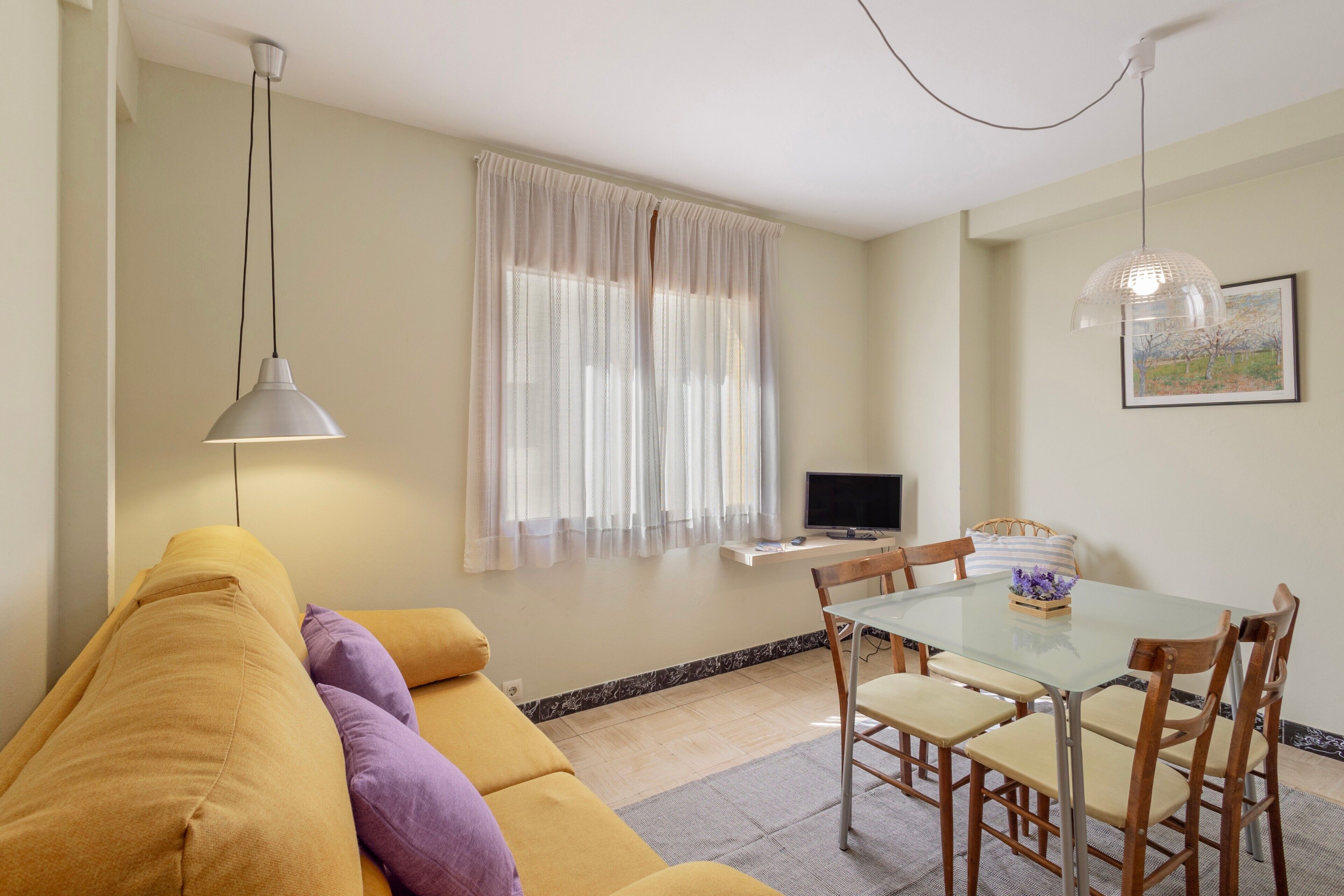 A living area with a sofa, a dining table with chairs, a TV, and a window with curtains.
