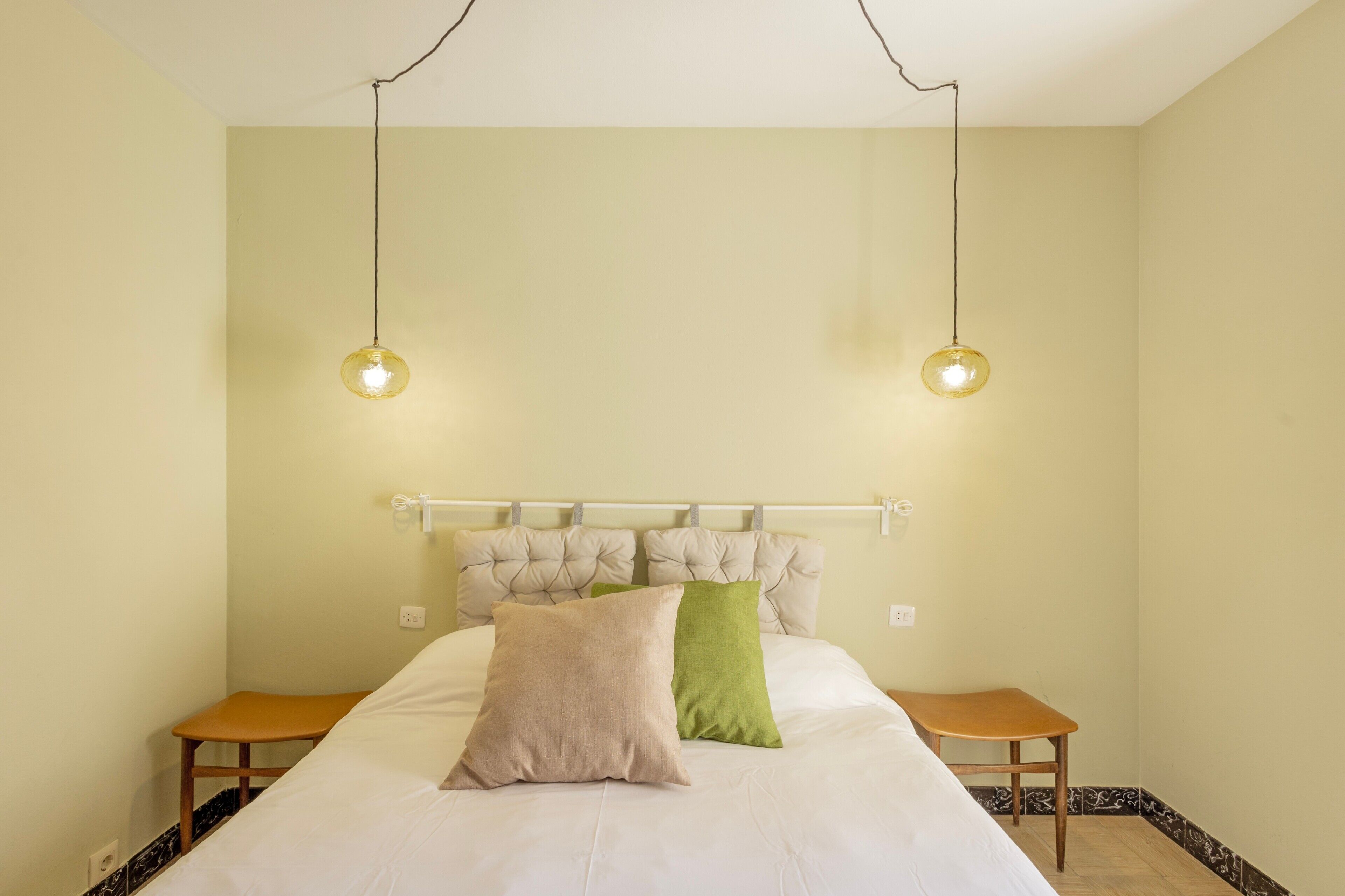 Een slaapkamer met een bed, twee nachtkastjes, een hoofdeinde en twee hangende lampen.