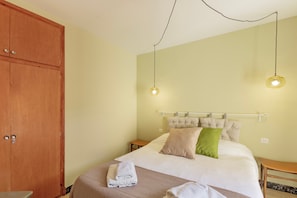 A bedroom with a bed, pillows, a wooden wardrobe, and a bedside table.