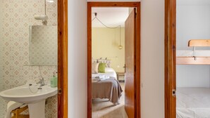 Un pasillo estrecho que conduce a un dormitorio con literas, una mesita de noche y una lámpara colgante.