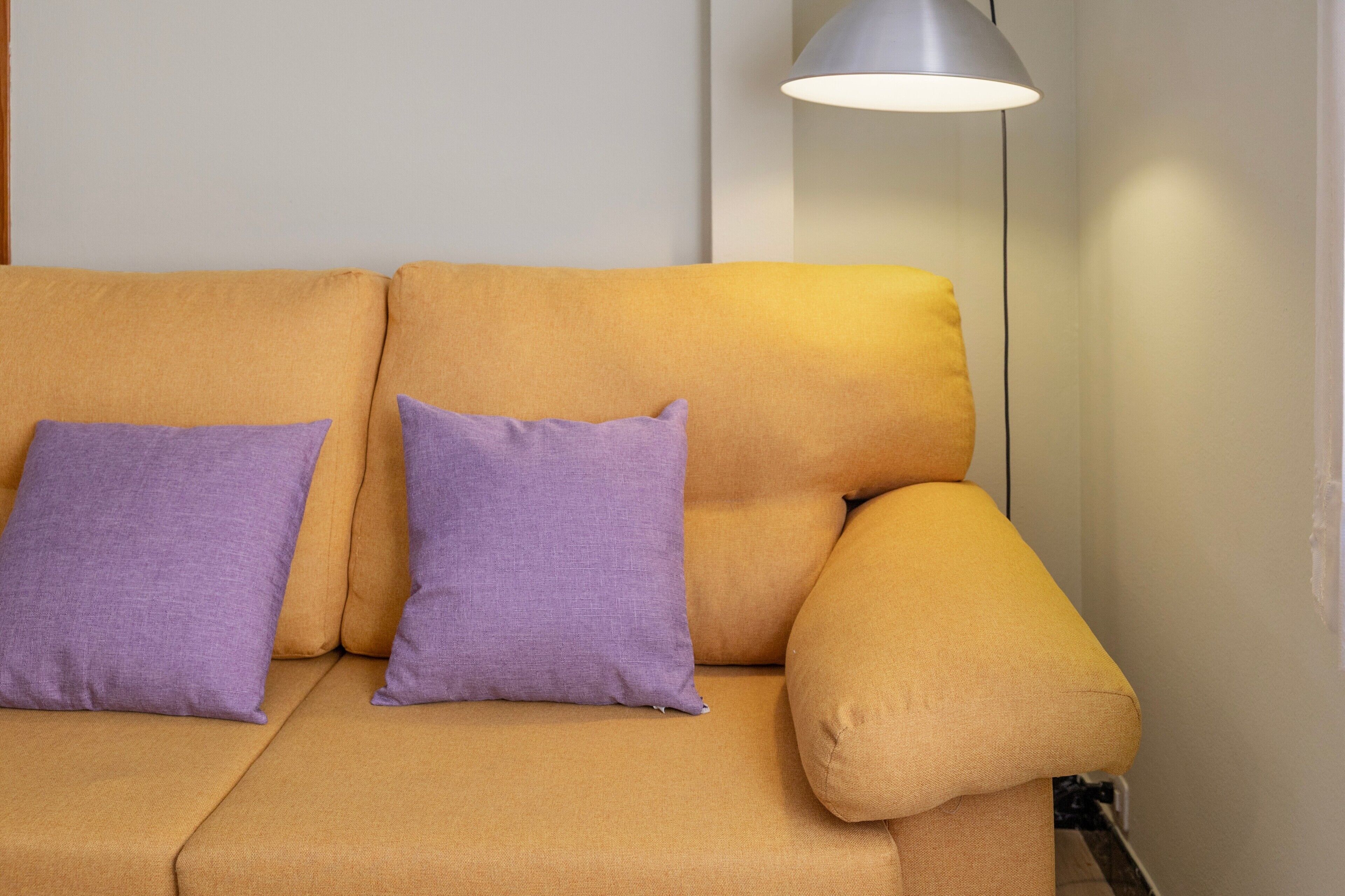 Un sofá con dos almohadas moradas y una lámpara de pie.
