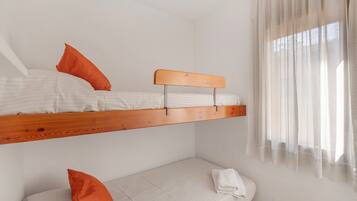 A bunk bed with a wooden headboard, a single bed below, and a window with sheer curtains.
