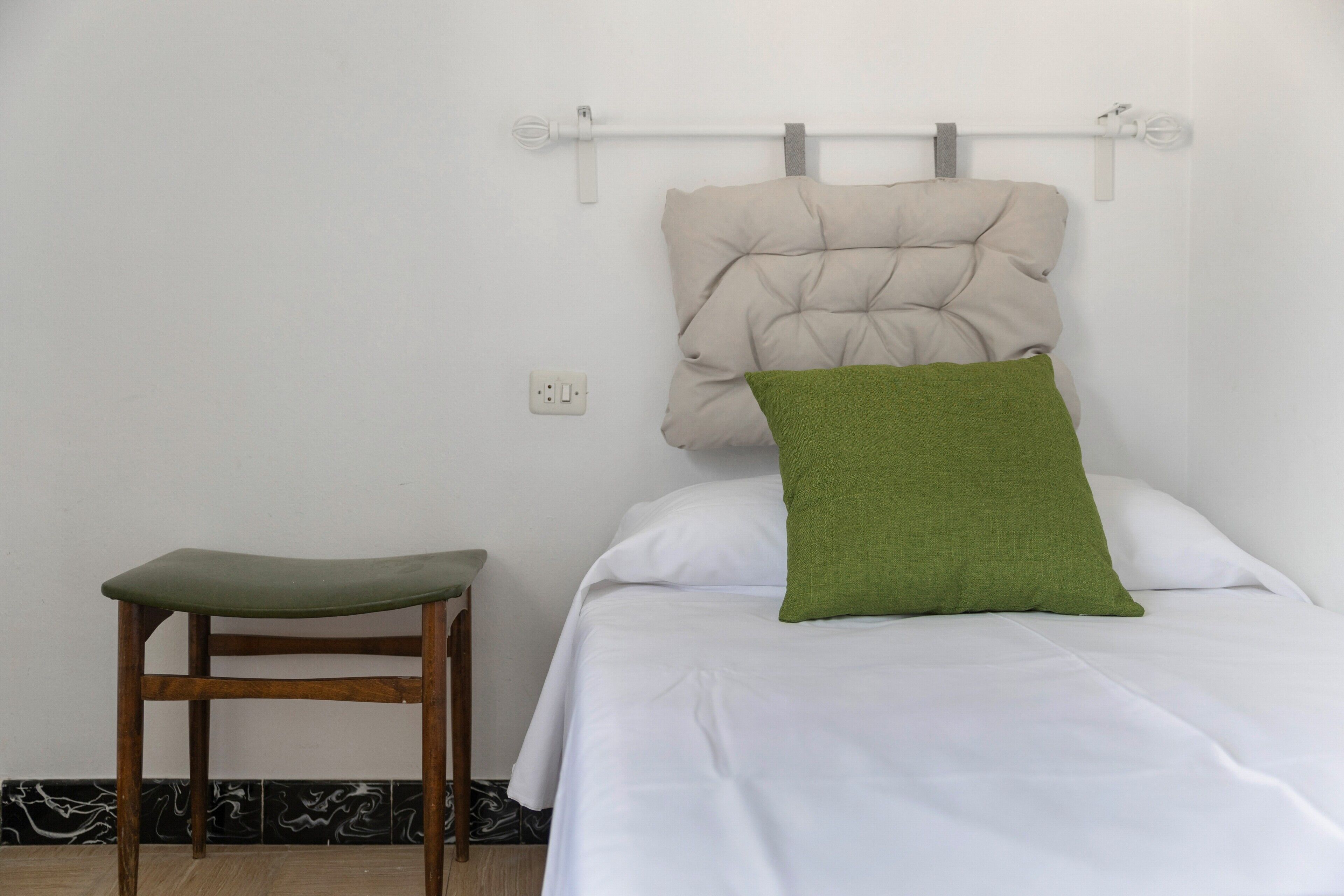 A bed with a headboard, a green pillow, and a wooden chair.