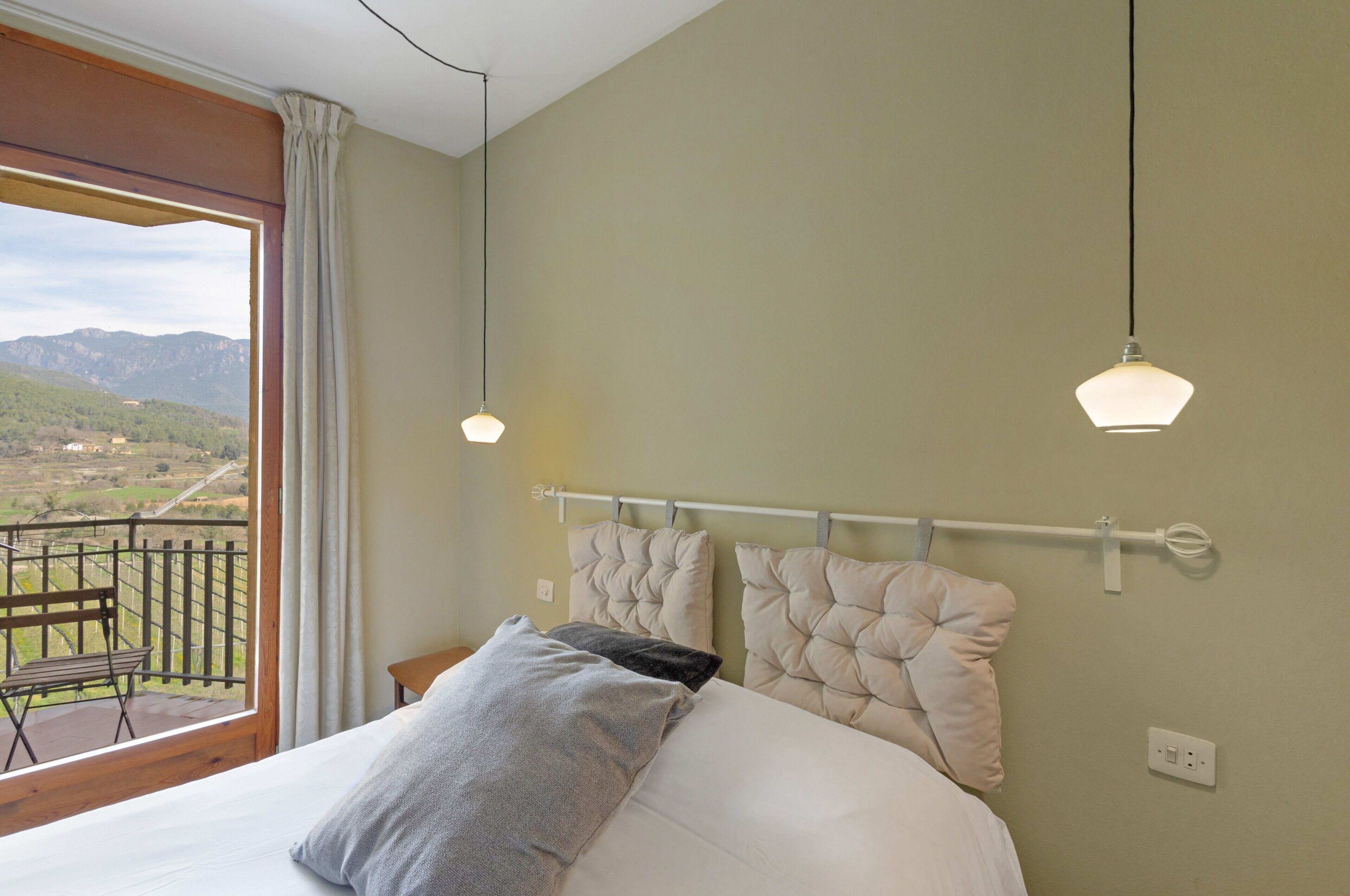Een slaapkamer met een bed, twee kussens, een nachtkastje, een raam met uitzicht op bergen, en twee hanglampen.