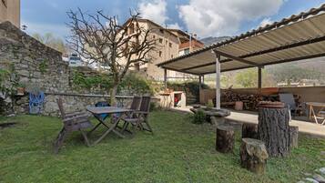 Un área de estar al aire libre techada, con una mesa, sillas, un muro de piedra y un árbol.