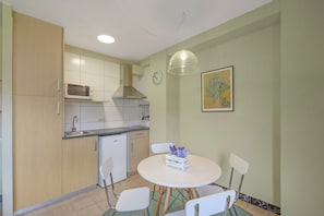A kitchen with a microwave, sink, and stove, a dining table with chairs, and a wall clock. - Apartment 'La Canal' with Mountain View, Private Terrace and Wi-Fi (Sant Llorenc de Morunys)