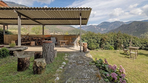 A covered outdoor seating area with a view of mountains, wooden furniture, and a stone pathway. - Apartment 'El Campanar' with Shared Garden and Wi-Fi (Sant Llorenc de Morunys)