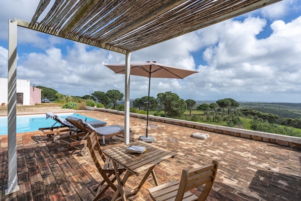 Una terraza en la azotea con piscina, sillones de descanso y una mesa con sombrilla.
