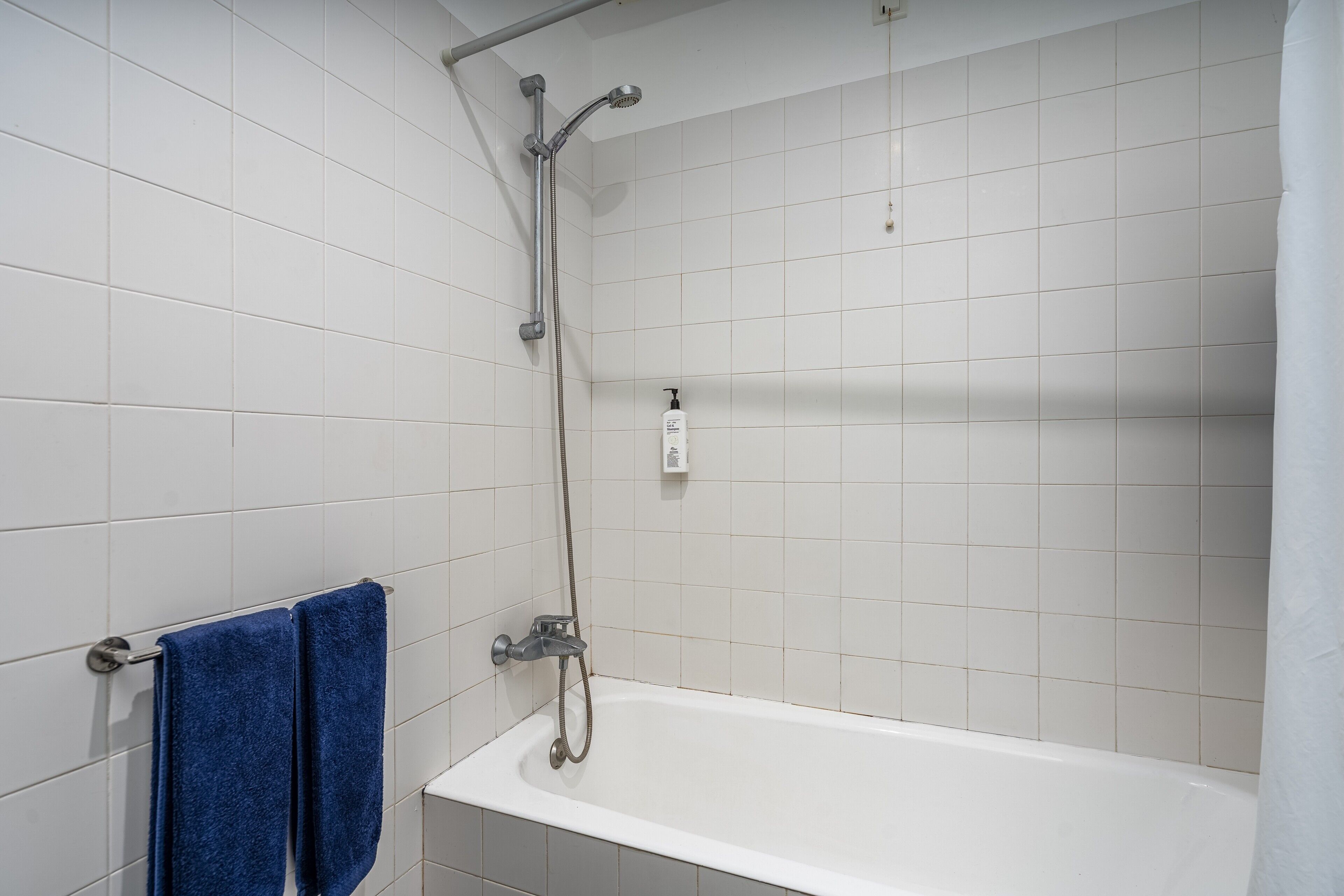 A bathroom with a bathtub, a shower, and a towel rack with blue towels.