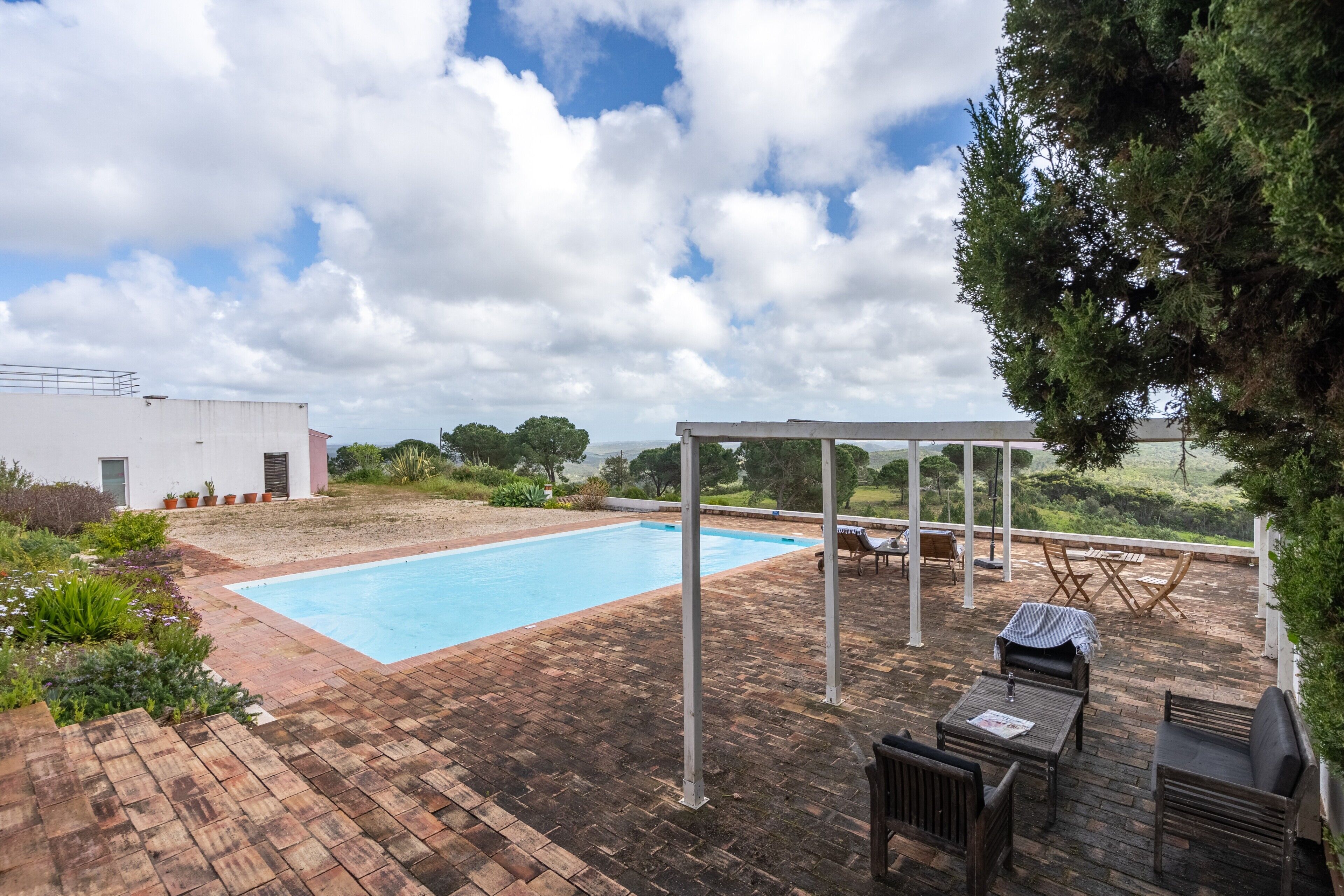 Une piscine avec un espace patio, du mobilier d’extérieur et une pergola.