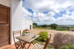 An outdoor patio with a wooden table and chairs, a bottle, and two cups.