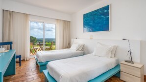 Habitación de hotel con dos camas, un escritorio, una silla, una mesita de noche y un ventanal con vistas.