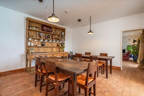 A dining area with a wooden table and chairs, a bookshelf with various items, and hanging pendant lights.