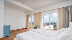 A hotel room with a large bed, a small table, and a view of the city through large windows. - Room 'Maio' with Sea View, Shared Pool and Wi-Fi (Bordeira)
