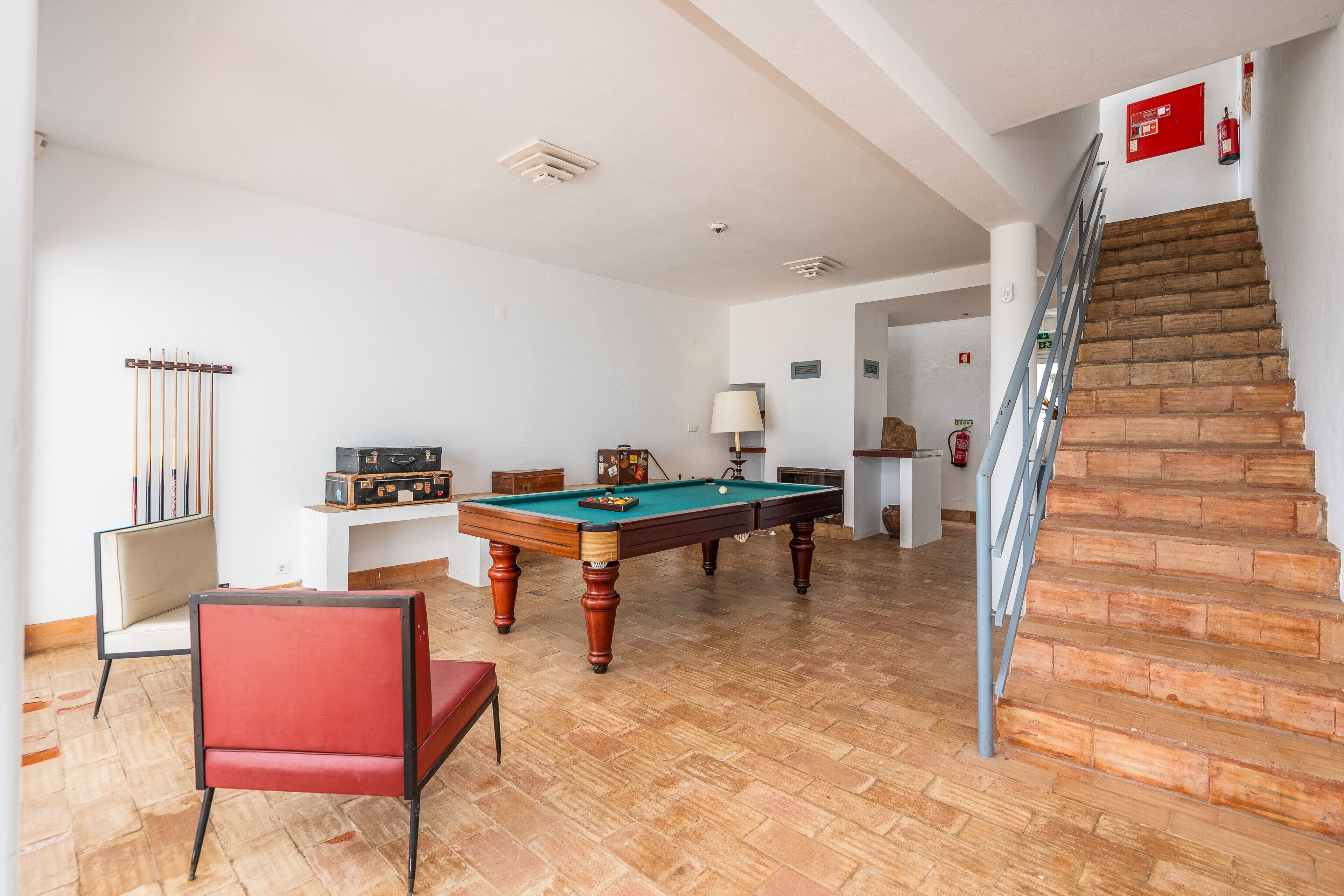 A room with a pool table, a red chair, a staircase, and a fire extinguisher.