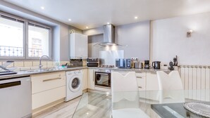 Een moderne keuken met vaatwasser, wasmachine, oven, magnetron en een eethoek met een glazen tafel en stoelen.