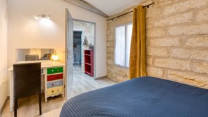 Een slaapkamer met een bed, een bureau met lades, een stoel, een lamp, een kledingkast en een raam met gordijnen.