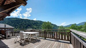 A wooden deck with a table and chairs, overlooking a forested mountain.