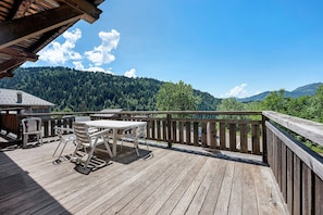 A wooden deck with a table and chairs, overlooking a forested mountain.