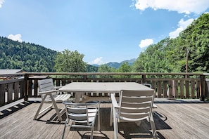 Eine Holzterrasse mit Tisch und StĂŒhlen mit Blick auf eine bewaldete Berglandschaft.